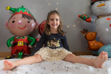 Cute little girl sitting on the play mat with funny expression. Christmas balloon and lights decoration in the background