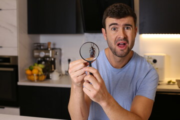 Shocked man observing a cockroach through magnifying glass