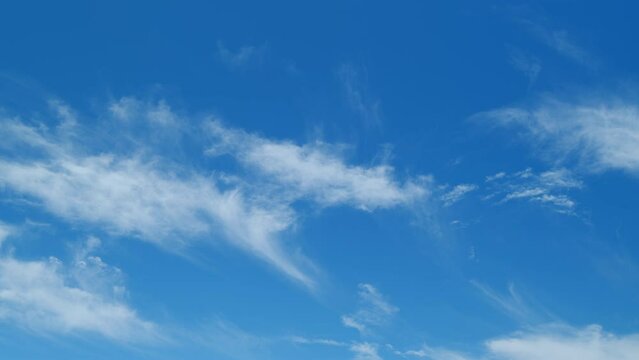 Wispy cirrus clouds pass over blue sky in nature. Elongated cirrus clouds move across sky. Time lapse.