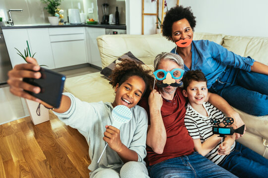 Happy family with party props taking selfie by smartphone sitting on sofa at home