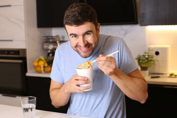 Cute guy eating instant noodles in the kitchen
