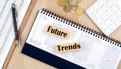 FUTURE TRENDS word written on wooden block on planner with coins, clipboard and a calculator