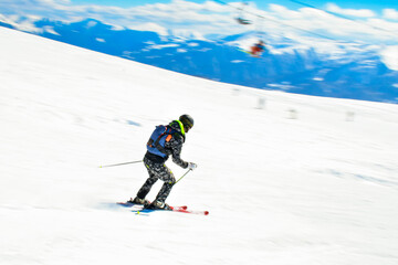 Fototapeta na wymiar Dynamic picture of a skier on the piste in Alps. Woman skier in the soft snow. Active winter holidays, skiing downhill in sunny day. Intentional blur filter effect