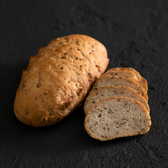 Round loaf of homemade white wheat bread with seeds with cut slices. Traditional family pastry. Fresh bread with crispy crust. Black background. Soft focus. Close-up. Copy space.