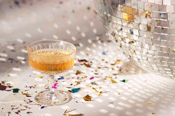 Champagne glass with golden bubbles make cheers on sparkling white and silver disco ball background...
