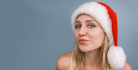 Christmas vacation. Portrait of young cheerful woman in santa hat and summer clothes celebrating Christmas on equator. Girl smiles looking at camera on light gray background. Vacations, travel.