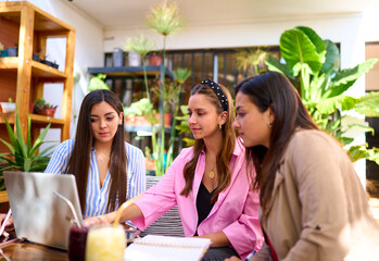 three young latin women entrepreneurs with  laptop working in a cafe on their online marketing business - obrazy, fototapety, plakaty