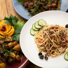 Italian pasta with minced meat and parmesan cheese. Dish is served on white plate with cucumbers and olives. Italian cuisine. Soft focus. 