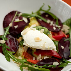 Portion of salad with beets, peppers, arugula, lettuce and cream cheese in white plate. Healthy lifestyle. Healthy nutrition. Top view. Vegetarian food. Close-up. Soft focus.