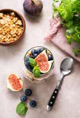 Natural yogurt with muesli, figs and berries in a glass on a pink background with mint.