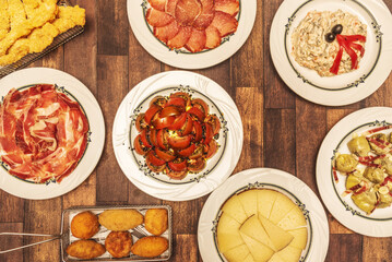 Large set of dishes of Spanish gastronomy and varied tapas with croquettes, tomato salad, chorizo loin, Russian salad, sempiterna tapa of knife-cut acorn-fed Iberian ham and cured sheep cheese