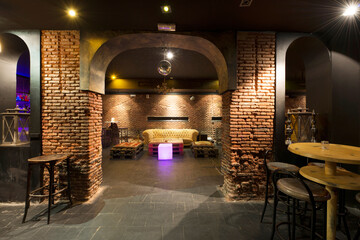 A late-night cocktail bar with vintage exposed brick walls, high tables with stools, and rooms with...