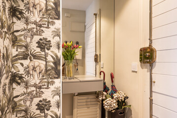 Small hall of a house with a mirror on the wall, decorative wallpaper and a full umbrella stand