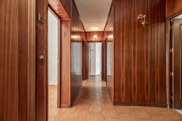 lobby of a house with all the walls covered in wood, access to several rooms, golden wall lights...