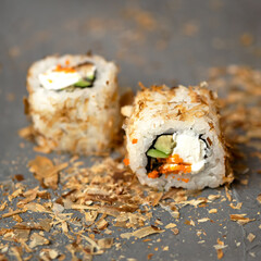 Sushi rolls close up. Two rolls are rolled in fish shavings. Rolls with avocado, cucumber, cream cheese and caviar. Healthy diet. Vegetarian food. Dark gray background. Soft focus.
