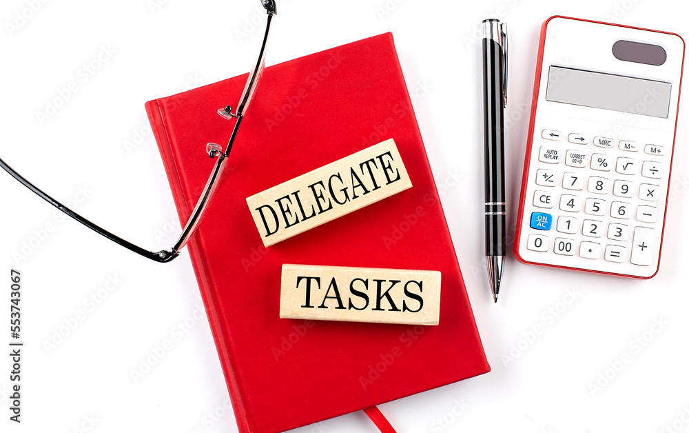 Aufkleber delegate tasks text on wooden block on red notebook