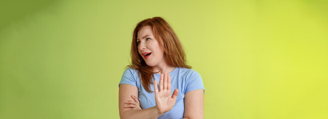 Enough wasting my time. Ignorant uninterested redhead mature woman turn away displeased reluctant show stop no gesture hold palm refusal rejecting unpleasant offer green background