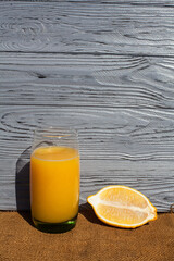 A composition of fresh fruit and drink, lemon around an orange juice in a glass, on a dark textured...