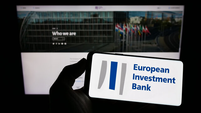 Stuttgart, Germany - 11-30-2022: Person holding mobile phone with logo of EU institution European Investment Bank (EIB) on screen in front of web page. Focus on phone display.