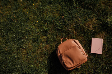 A school bag and a notebook on the grass on green backgroud