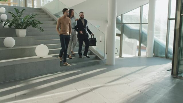 Long shot of group of business people talking to each other while going down the stairs after working day