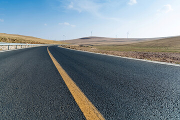 Empty asphalt highway road surrounded by fields with windmills