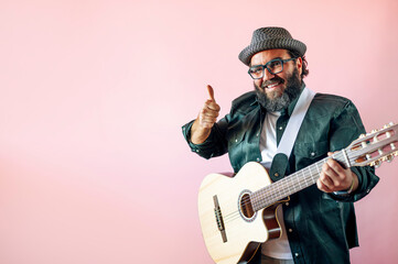 Happy bearded man playing acoustic guitar over pink background. He raises his finger as a symbol of possible.