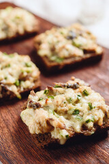Rye bread toast with smoked mackerel, cream, cheese and green onion on wooden cutting board. Delicious appetizer, tapas. Selective focus - 553753437
