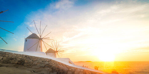 famous windmill of Mykonos island and The Town over seascape with sunset sun, Mykonos island, Greece, toned