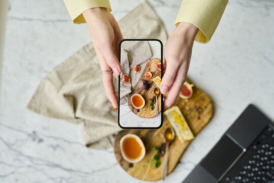 High angle view of young woman photographing food on wooden tray using her smartphone