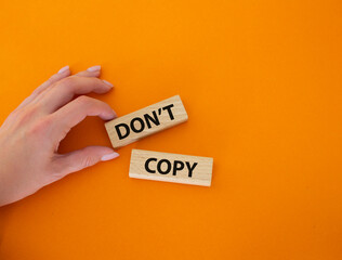 Don't copy symbol. Wooden blocks with words Don't copy. Beautiful orange background. Businessman hand. Business and Don't copy concept. Copy space.