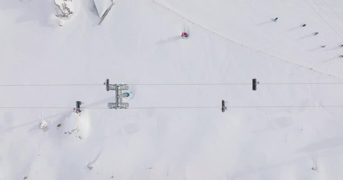 Chairlift from above, ski resort in the Alps, people skiing and riding chairlift uphill. Winter landscape in the Alps