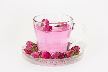 Pink tea in a transparent glass mug and small pink rose buds on a white background