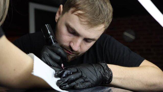 Tattoo master is tattooing a woman's hand. Wireless tattoo machine, safety and hygiene at work. Close-up of tattoo artist work. Tattoo salon