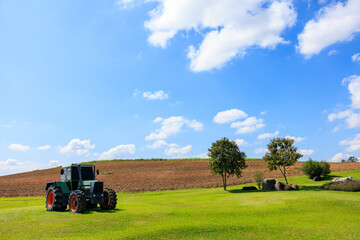 old tractor in the agriculture farmland on the green grass blue sky background,
