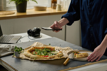 Close-up of photographer making close-up portrait of delicious pizza on her smartphone during work in studio