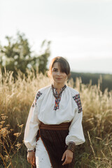 Young woman in traditional national embroidered shirt and skirt on nature at sunset. Ethnic national clothes style, embroidered shirt.