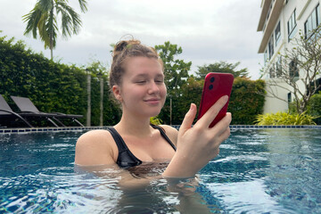 Young happy girl, beautiful woman is using cell mobile phone, looking at smartphone in water in...