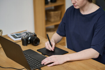 Young designer using tablet to retouch photo on laptop after shooting, she sitting at her workplace in studio