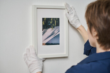 Rear view of young woman decorating white wall with framed photo