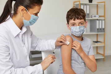Child in facemask gets flu or Covid 19 shot at modern clinic during mass compulsory vaccination campaign. Nurse or doctor gives shoulder injection to school boy to protect him from dangerous disease - obrazy, fototapety, plakaty