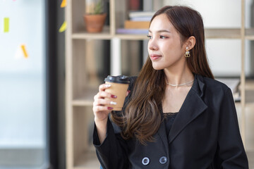 Happy Asian young woman drinking coffee while working online in office, employee freelance online marketing e-commerce telemarketing concept.
