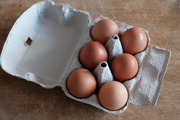 six organic eggs in egg box on wooden plate