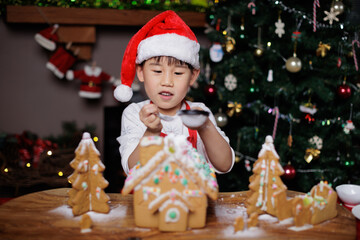 Fototapeta na wymiar young girl wearing Santa hat was decorating gingerbread house for celebrating Christmas at home