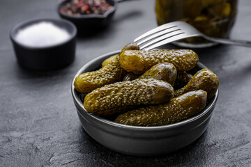 Bowl of pickled cucumbers and ingredients on black table, closeup