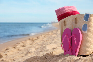 Summer bag with beach accessories on sand near sea, space for text