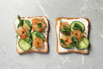 Tasty toasts with cream cheese, shrimps, cucumbers and microgreens on grey marble table, flat lay