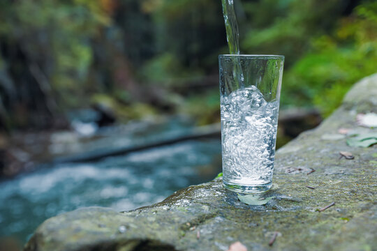 Fresh water pouring into glass on stone near stream. Space for text © New Africa