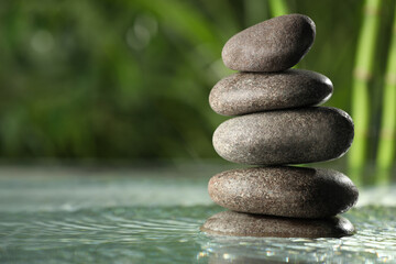 Stacked stones on water surface against bamboo stems and green leaves, closeup. Space for text