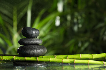 Stacked stones on bamboo stems over water against blurred background. Space for text